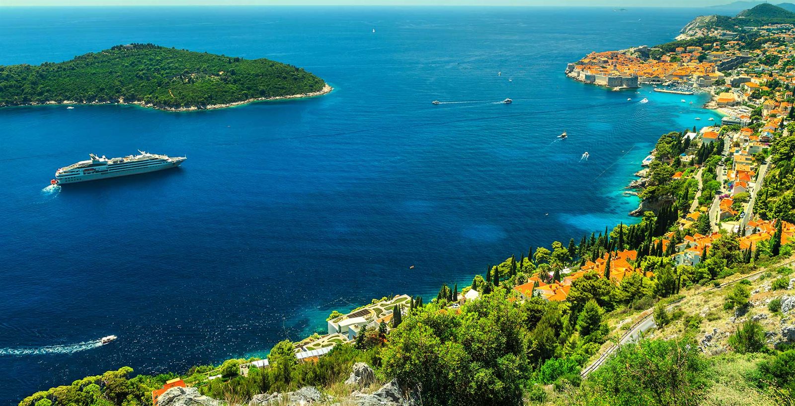 Cruise ship sailing past a green, rocky Mediterranean coastline